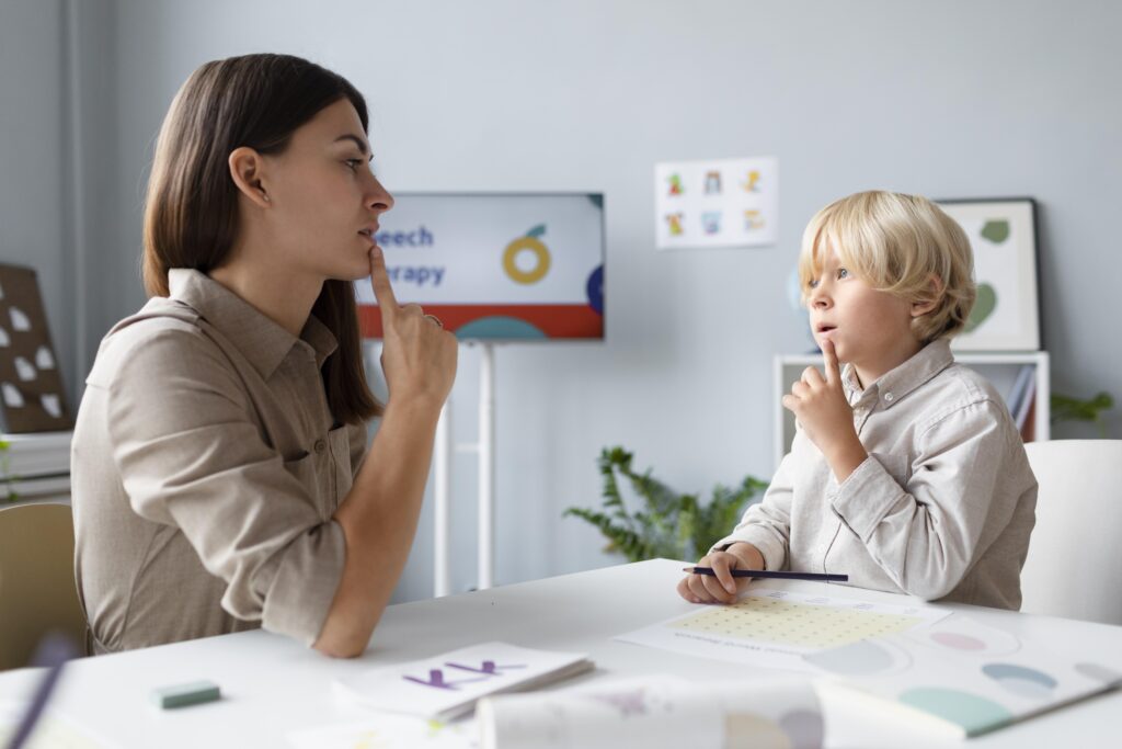 A female speech therapist and a young boy practice speech sounds together during a therapy session.