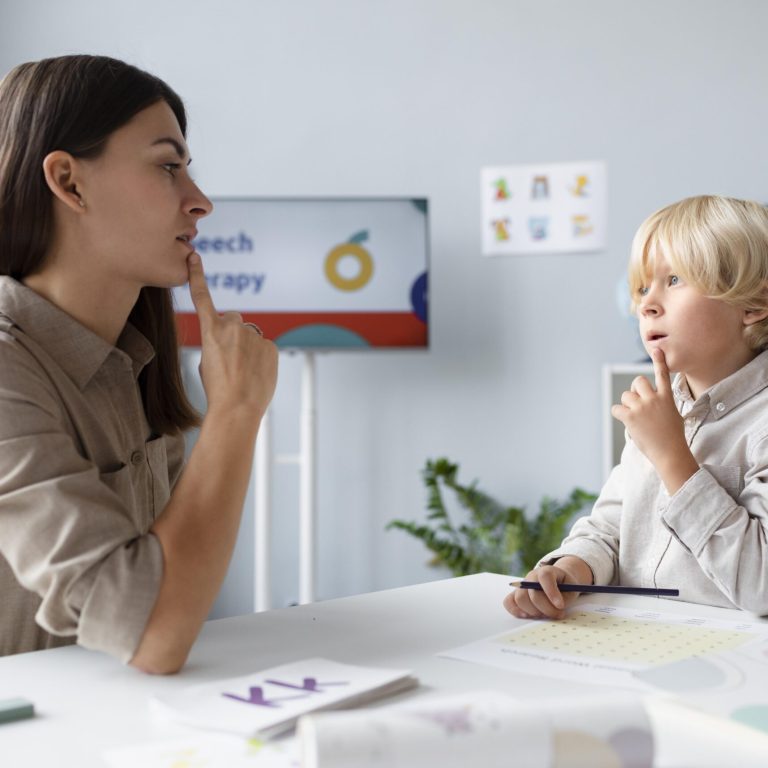 A female speech therapist and a young boy practice speech sounds together during a therapy session.